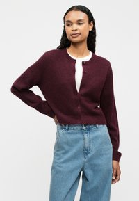 Burgundy knitted cardigan with a round neckline, button closure, and long sleeves, paired with light blue high-waisted jeans.