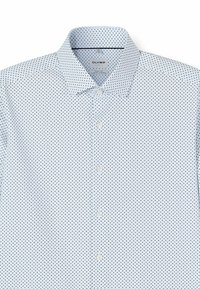 Weißes Hemd mit spitzem Kragen, kleinen schwarzen Polka-Dots und Knopfverschluss. Der Stoff hat eine glatte Textur und ein leichtes Design.