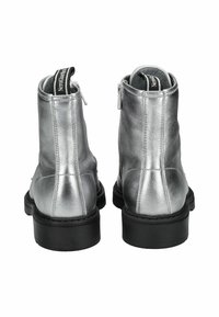 Bottines argentées avec une finition métallique lisse, une semelle en caoutchouc noir et une fermeture éclair sur le côté pour un enfilage facile. Doublées d'un intérieur en tissu.