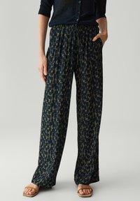 Pantalons larges à motifs navy avec une taille élastique et un cordon de serrage. Le tissu a une texture douce avec des formes géométriques vert olive.