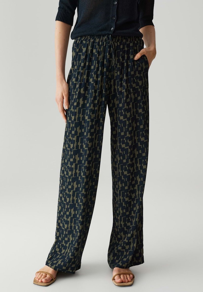 Pantalons larges à motifs navy avec une taille élastique et un cordon de serrage. Le tissu a une texture douce avec des formes géométriques vert olive.