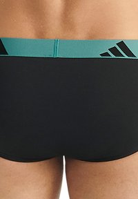 Černé plavky s tyrkysovým pasem; obsahují logo Adidas a horizontální švy podél pasu. Hladká struktura tkaniny.