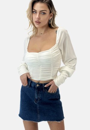 Top bianco corto con design arricciato e maniche lunghe abbinato a una mini gonna di jeans blu scuro con tasche frontali e orlo sfrangiato.