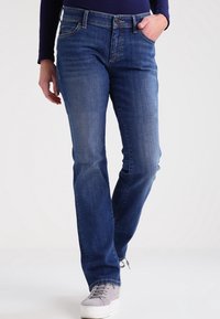 Jeans in denim blu con taglio dritto, caratterizzati da un classico design a cinque tasche e un leggero sbiadimento. Abbinati a sneakers grigie.