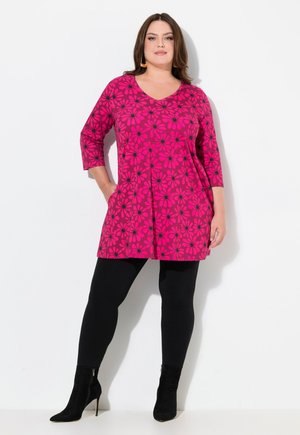 Pink tunika med sort blomstermønster, med V-udskæring og trekvartærmer, parret med sorte leggins og ankelstøvler.