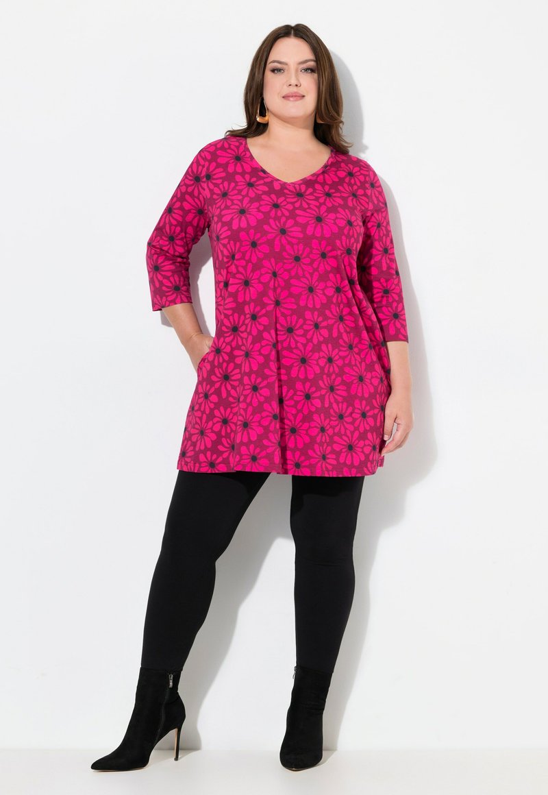 Pink tunika med sort blomstermønster, med V-udskæring og trekvartærmer, parret med sorte leggins og ankelstøvler.