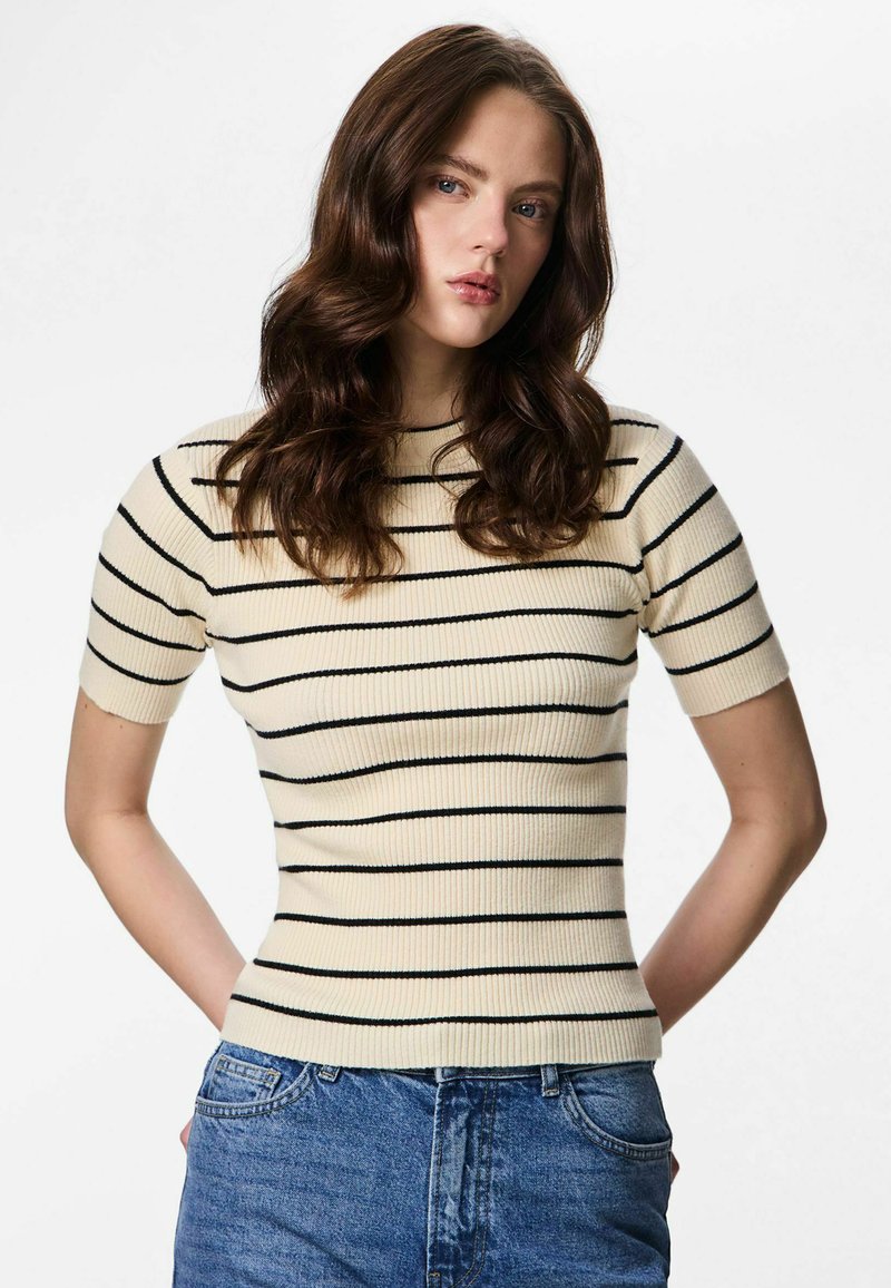 Haut court à manches courtes crème côtelé avec des rayures horizontales noires, coupe ajustée et encolure ronde, porté rentré dans un jean en denim bleu.