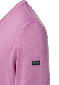 Nahaufnahme eines fliederfarbenen Strickpulloverarms mit einem schwarzen, rechteckigen Stoffetikett "MAERZ München", das nahe der Schulter eingenäht ist.