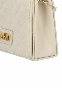 Borsa a tracolla beige trapuntata con hardware dorato. Caratterizzata da una forma strutturata, placca con logo e una tracolla a catena. Esterno in pelle liscia e testurizzata.