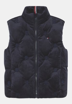 Marineblå polstret vest med høj krave, lynlås foran, quiltede logomønstre og lille rød, hvid og blå flagemblem på brystet.