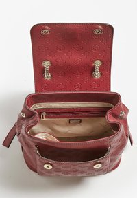 Sac à dos en cuir rouge avec motif de logo embossé, fermoirs à pression dorés, détails de chaîne, et doublure intérieure beige avec poche zippée.