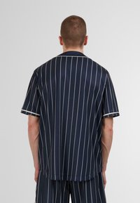 Camisa de manga corta a rayas marinas en una tela suave y ligera. Rayas blancas verticales y un corte relajado con dobladillo redondeado.