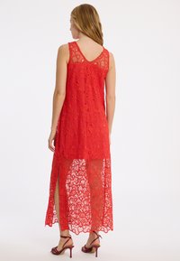 Rotes Spitzen-Maxikleid mit ärmellosem Design, V-Ausschnitt, offenem Rücken und einem transparenten, floralen Muster mit Seitenschlitzen.