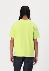 Short-sleeve, crew neck t-shirt in fluorescent green cotton. Features a relaxed fit and tag at the hem. Worn with dark blue jeans.