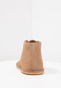 Stivaletti alla caviglia beige in suede con punta arrotondata, caratterizzati da una suola cucita e un tacco basso, che mostrano una trama morbida e liscia.