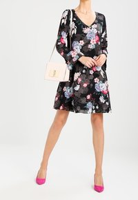 Kukkallinen musta mekko, jossa on pitkät hihat ja V-pääntie. Sisältää vaaleanpunaisia ja sinisiä kukkia, yhdistettynä vaaleaan käsilaukkuun ja kirkkaan vaaleanpunaisiin korkokenkiin.