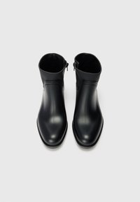 Pair of black ankle boots with zippers on the inner sides, smooth finish, and rounded toes on a white background.