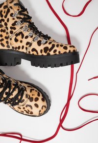 Bottes chunky à imprimé léopard avec des lacets noirs, quincaillerie argentée et semelles épaisses noires. Des lacets rouges sont enroulés autour de l'image.