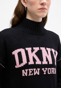 Czarny sweter z dzianiny z wysokim, ribbowanym kołnierzem i dużym różowym napisem "DKNY NEW YORK", z teksturowanym detalem materiału.