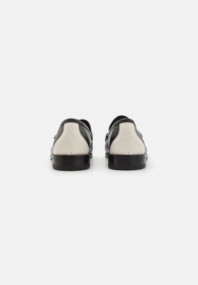 Black and white leather shoes with a rounded shape, featuring contrasting heel and side accents, smooth texture, and a low profile sole.