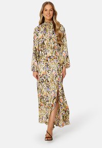 Longue robe maxi florale avec un col haut, des manches bouffantes, une fente sur le côté et un motif coloré de fleurs sur un fond jaune.