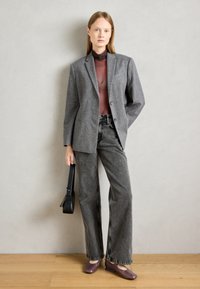 Gray wool blazer with two buttons, paired with a sheer brown top and high-waisted black jeans. Finished with purple flats and a black bag.