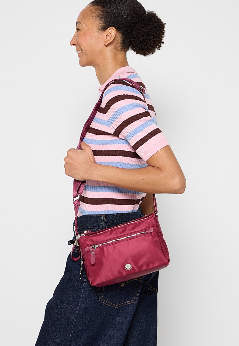 Bolso bandolera de nailon burdeos, de forma rectangular, que cuenta con un bolsillo frontal con cremallera y una correa ajustable. Textura suave con acentos de hardware mínimos.