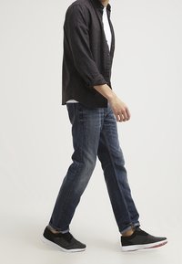 Camisa negra de botones sobre una camiseta blanca, jeans azules y zapatillas deportivas negras con suelas blancas. Enfóquese en un ajuste y estilo casual y relajado.