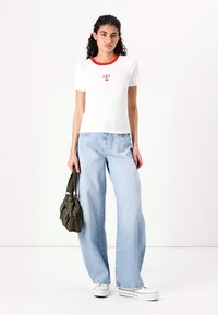 White short-sleeve GAP t-shirt with red neckline, paired with light blue wide-leg jeans and a dark green bag. White sneakers complete the outfit.