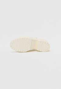 Semelle de sneaker blanche avec un motif de semelle texturé et un talon légèrement surélevé. Fabriquée en caoutchouc avec des zones lisses et rainurées.