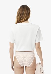 T-shirt bianco cropped, maniche corte, in morbido cotone. Intimo rosa in pizzo con motivo floreale, vita elastica, finitura liscia.