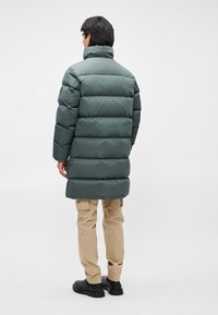 Puffatakki tumman vihreänä, keskikokoisena ja vaakasuoralla kudontamallilla. Mukana korkeakauluksinen ja yhdistetty beigeihin cargo-housuihin sekä mustiin kenkiin.