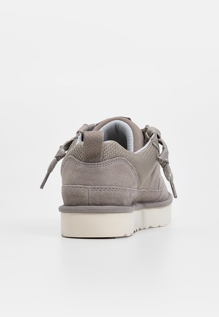 Grijze suède sneaker met een gewatteerde kraag, ronde veters en een witte rubberen zool. De hak heeft een gestructureerd paneel en stikseldetails.
