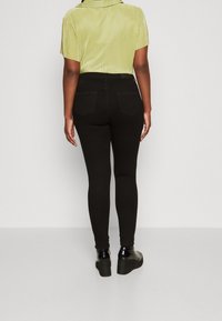 Jeans negros ajustados con cintura alta, con una textura suave y bolsillos traseros. Combinados con una blusa corta de manga corta en verde claro y con relieve.