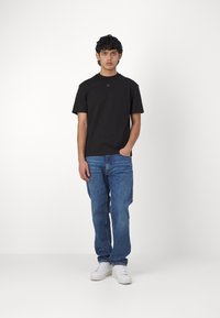 Svart T-skjorte med korte ermer og rund hals, med en liten logo, sammen med blå rettbente jeans og hvite joggesko.