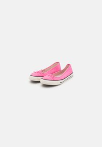 Zapatillas de lona rosa tipo slip-on con detalle de lazo, suelas de goma blanca y una franja negra en contraste a lo largo del borde. Textura suave en toda su superficie.