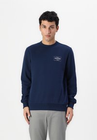 Sudadera azul marino hecha de mezcla de algodón, con un cuello redondo, puños de canalé y un pequeño parche de logo en el pecho.