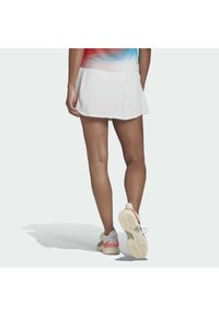 Witte sportrok met een uitlopende zoom. G gedragen met meerkleurige sportschoenen met grijze, rode en witte accenten. Soepele stofstructuur.