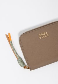 Brown fabric wallet with gold logo "BIMBA Y LOLA," zip closure, and a green braided strap with orange accents. Smooth texture.