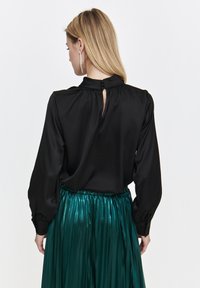 Black satin blouse with long sleeves and a keyhole back detail, paired with a green pleated metallic skirt featuring an elastic waistband.