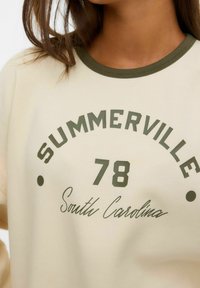 Sweatshirt couleur crème avec col ribbed vert foncé, arborant "SUMMERVILLE 78" et "Caroline du Sud" imprimés en texte contrasté.