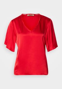 Blouse rouge en satin à manches courtes avec un col en V et une texture lisse et brillante sur un fond uni.
