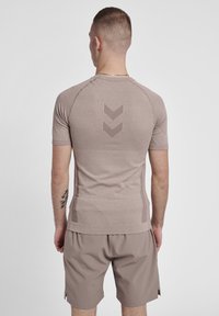 Camiseta atlética de manga corta en tono beige con una tela texturizada y un diseño en chevron en la parte trasera. Combinada con pantalones cortos beige a juego, que presentan un ajuste relajado.