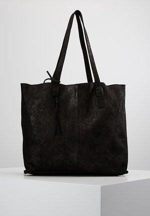 Sac cabas en cuir noir avec deux anses d'épaule et un détail pompon, présenté sur un piédestal blanc sur un fond gris clair.