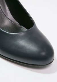 Pompe en cuir bleu foncé avec une texture lisse, bout pointu et un design dégagé qui révèle le pied. Silhouette minimaliste et élégante.