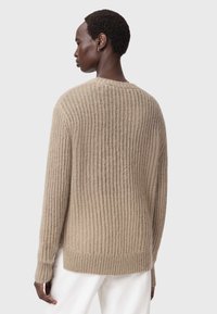 Pulover bej tricotat cu dungi, mâneci lungi și croială lejeră. Are un decolteu rotund și un finisaj moale, texturat.