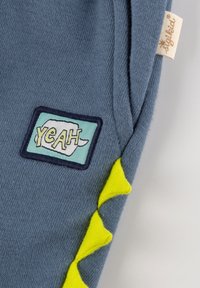 Light blue fabric with a patch displaying "YEAH" in yellow and green. Features a bright yellow zigzag accent along the side.