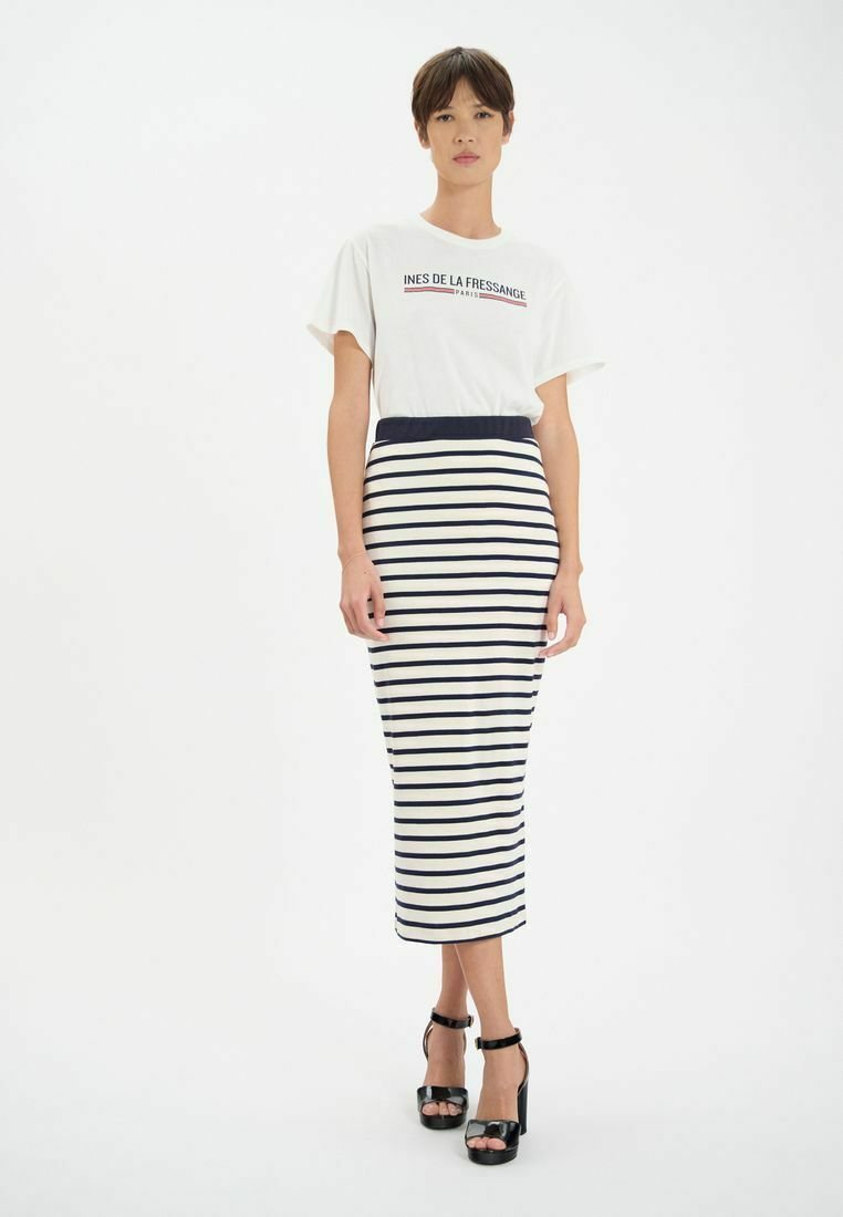 T-shirt blanc avec logo, associé à une jupe midi rayée en marine et crème. Présente une coupe ajustée et des talons hauts.