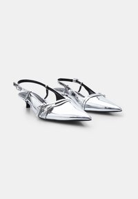 Srebrne metalne slingback čevlje s koničastim nosom in nizko blokasto peto, ki imajo več dekorativnih trakov čez zgornji del.