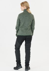 Grön, strukturerad tröja med hög krage, ihop med svarta, tajta byxor och svarta stövlar. Materialet i sweatshirt är mjukt och varmt.